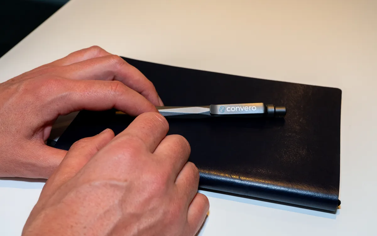 Hands holding a Convero-branded pen over a notebook